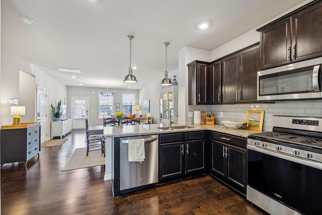 kitchen with light stone counters, dark wood-style flooring, a sink, appliances with stainless steel finishes, and backsplash