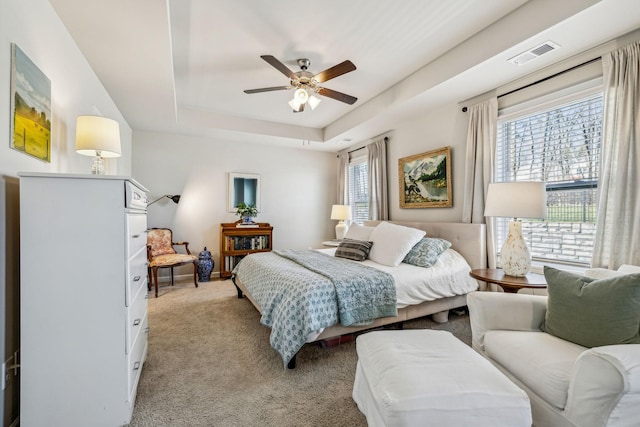 bedroom featuring ceiling fan, a tray ceiling, visible vents, and light carpet