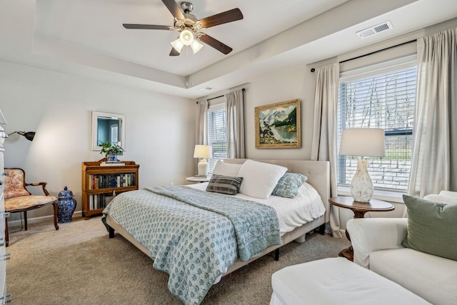 bedroom featuring visible vents, baseboards, a tray ceiling, carpet floors, and a ceiling fan