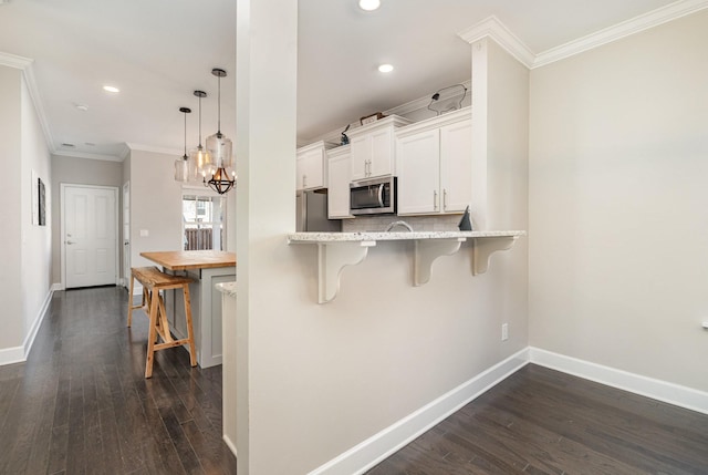 kitchen featuring backsplash, appliances with stainless steel finishes, a breakfast bar area, crown molding, and baseboards