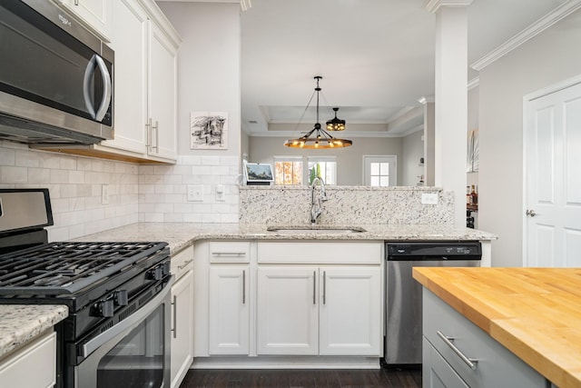 kitchen featuring butcher block countertops, ornamental molding, a sink, appliances with stainless steel finishes, and decorative backsplash