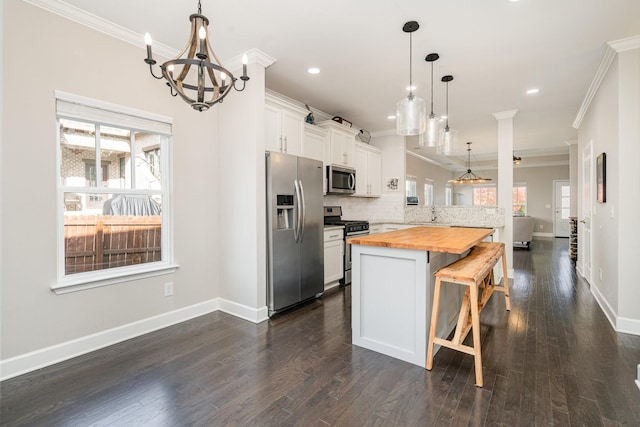 kitchen with ornamental molding, a kitchen breakfast bar, backsplash, appliances with stainless steel finishes, and butcher block counters