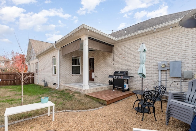 rear view of property with a deck, fence, a yard, a shingled roof, and brick siding