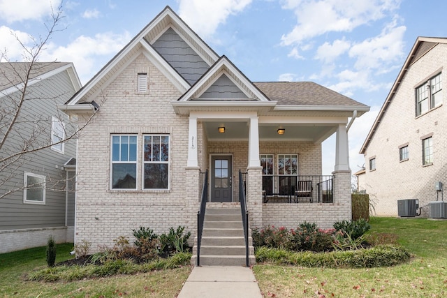 craftsman house featuring brick siding, covered porch, cooling unit, and a front lawn