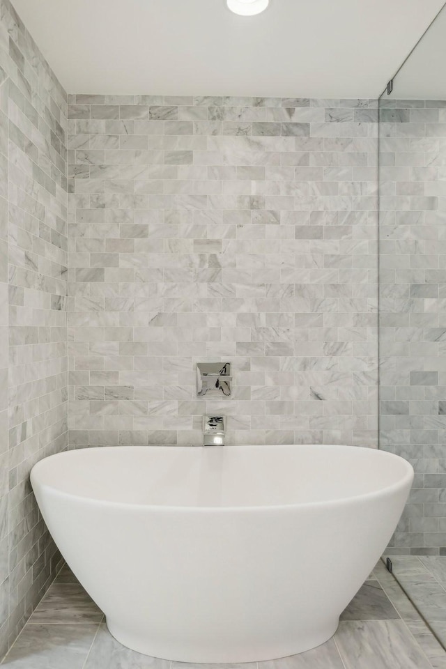 bathroom featuring marble finish floor, a freestanding bath, and tile walls