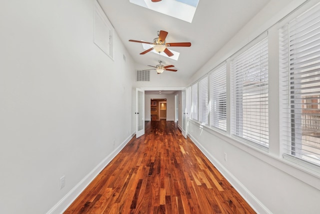 hall featuring visible vents, vaulted ceiling with skylight, baseboards, and wood finished floors