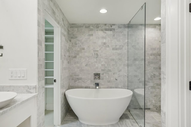 bathroom with marble finish floor, recessed lighting, tile walls, a soaking tub, and vanity