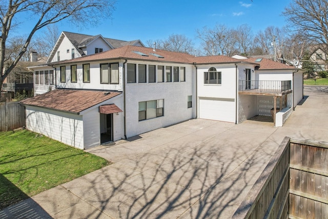 back of property with a lawn, concrete driveway, an attached garage, and fence