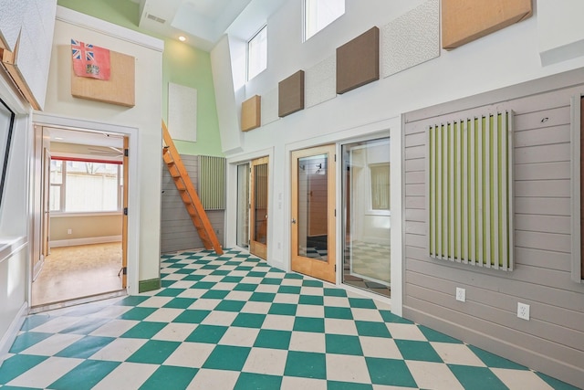 unfurnished room with tile patterned floors, stairway, wood walls, and a towering ceiling