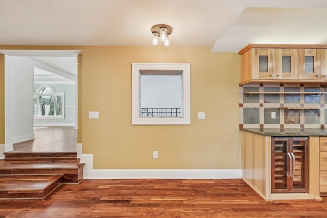 interior space featuring beverage cooler, tasteful backsplash, glass insert cabinets, and wood finished floors