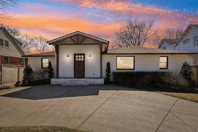 view of front of house with brick siding, a shingled roof, and fence