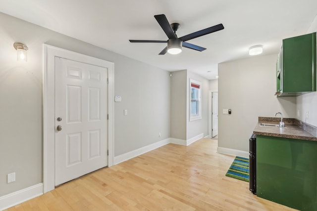 kitchen with dark countertops, green cabinets, baseboards, light wood-type flooring, and a sink