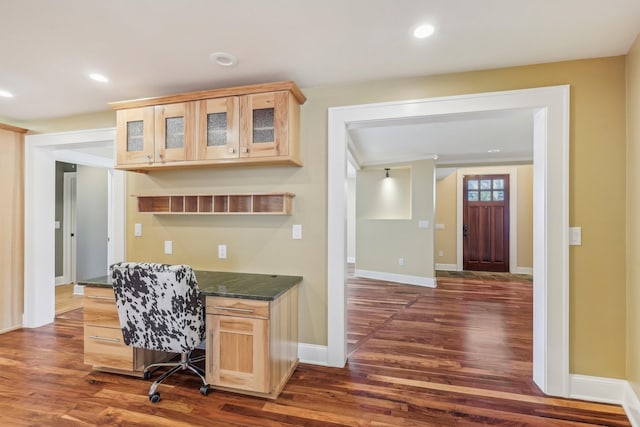 kitchen with dark wood-type flooring, recessed lighting, glass insert cabinets, and built in desk