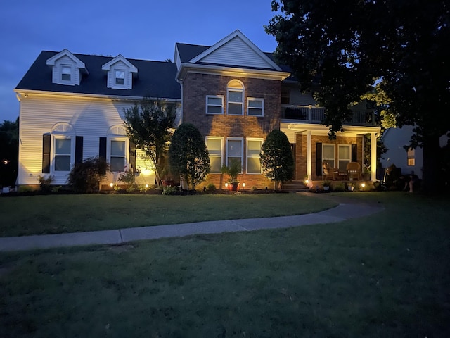 view of front of property with brick siding, covered porch, a front lawn, and a balcony