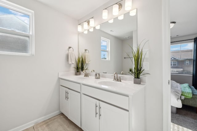 full bath with ensuite bath, double vanity, baseboards, and a sink