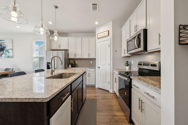 kitchen with visible vents, a center island with sink, a sink, wood finished floors, and stainless steel appliances