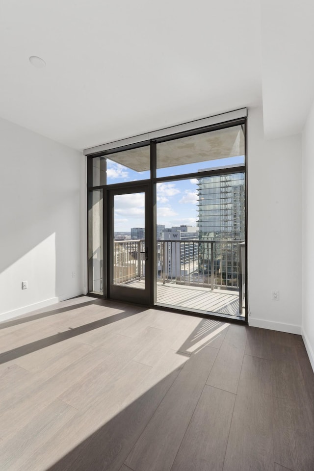 spare room with a view of city, wood finished floors, baseboards, and expansive windows