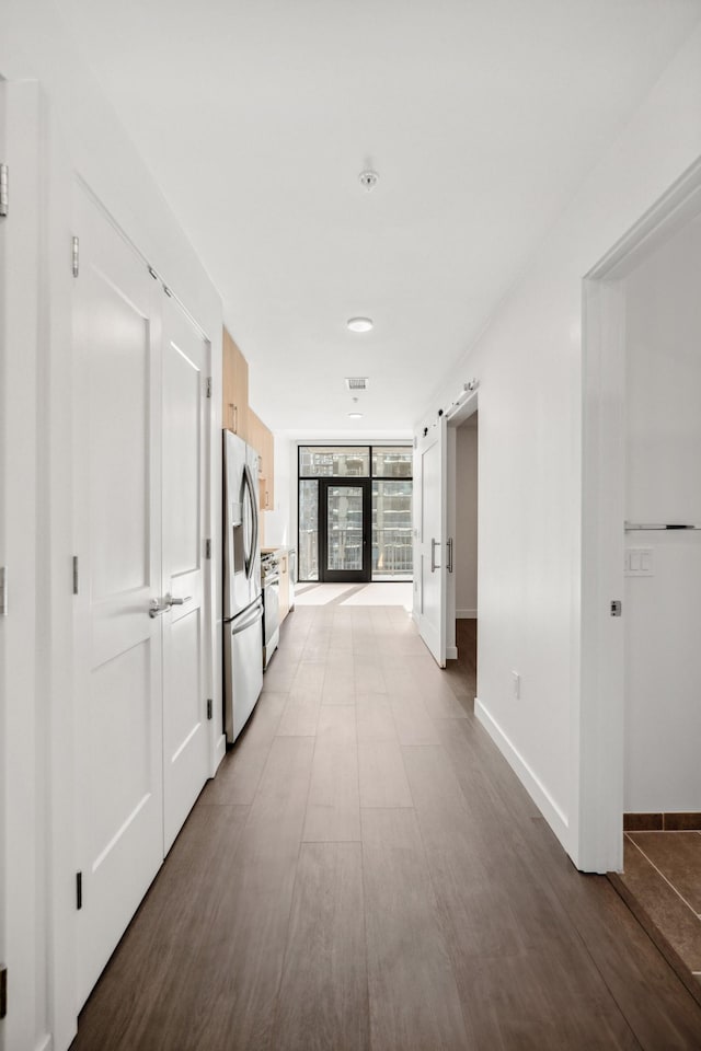 hallway with baseboards, a barn door, and wood finished floors