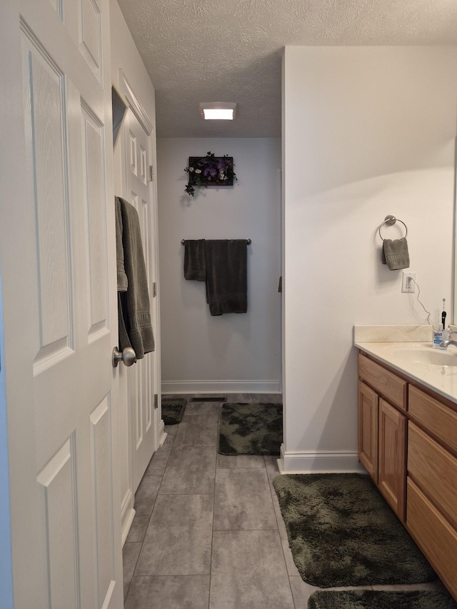 bathroom with tile patterned flooring, a textured ceiling, vanity, and baseboards