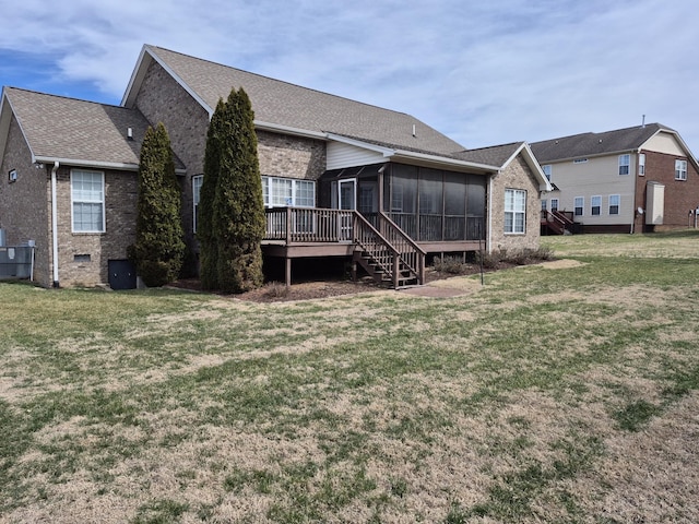 back of house featuring a lawn, a deck, a sunroom, a shingled roof, and brick siding