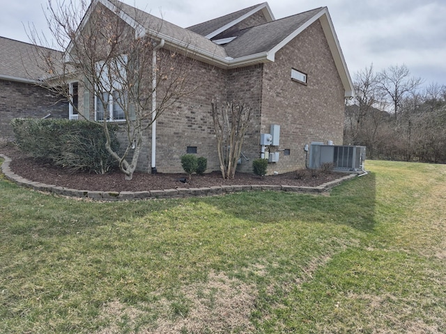 view of side of property with brick siding, central air condition unit, roof with shingles, a yard, and crawl space