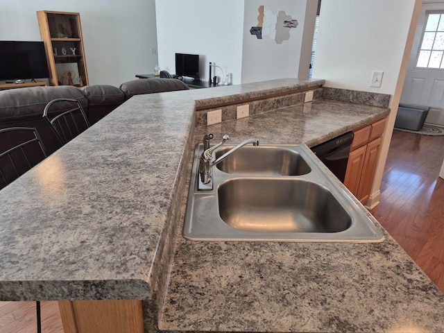 kitchen with open floor plan, black dishwasher, brown cabinets, wood finished floors, and a sink