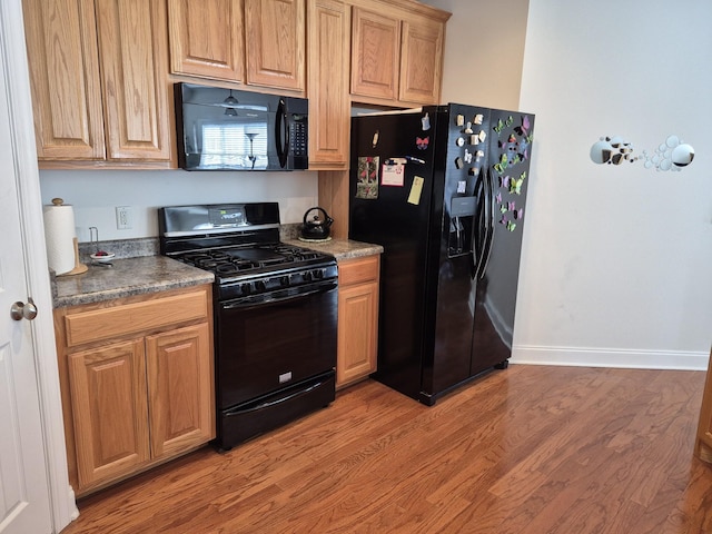 kitchen with dark countertops, baseboards, light wood-style floors, and black appliances