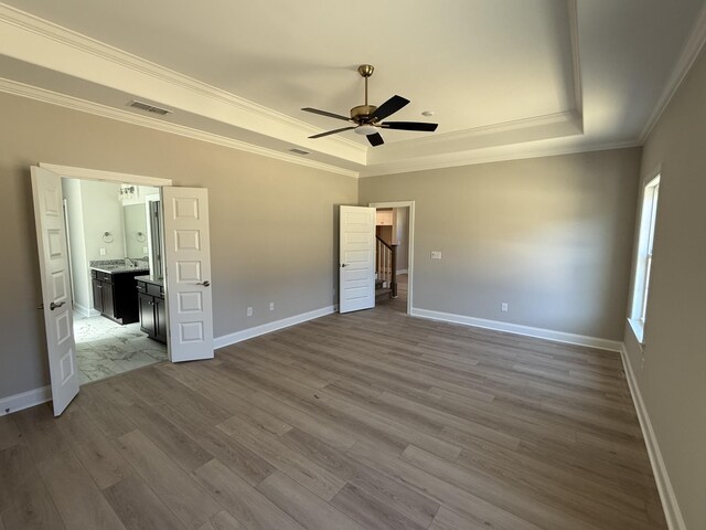 unfurnished bedroom with crown molding, a raised ceiling, baseboards, and wood finished floors