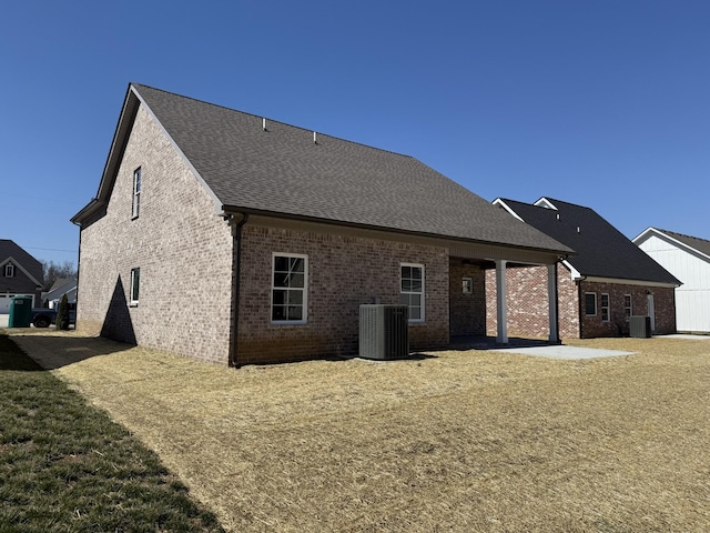 back of property with brick siding, central air condition unit, a shingled roof, and a yard