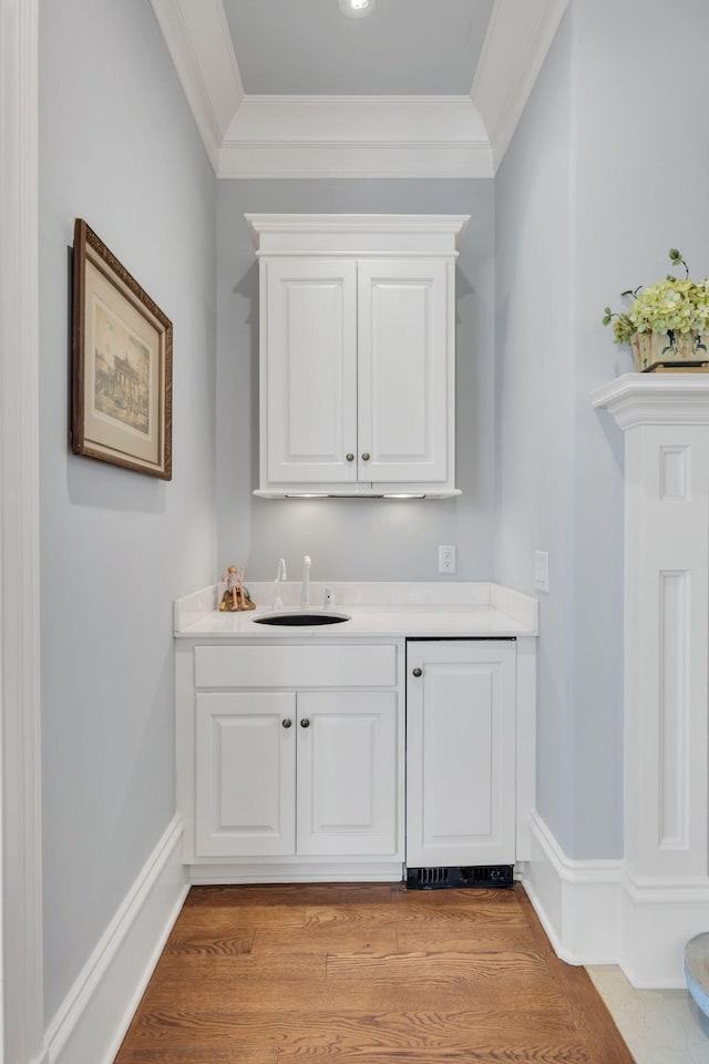 bar featuring ornamental molding, light wood-type flooring, baseboards, and a sink