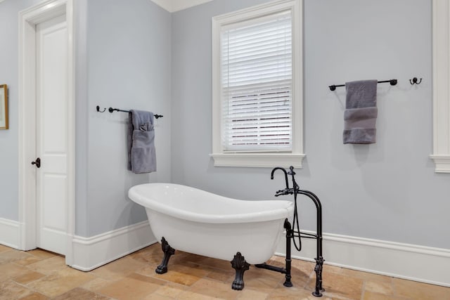 bathroom featuring a soaking tub, stone tile floors, and baseboards