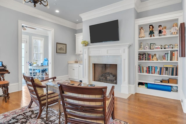 living area with built in shelves, light wood-style flooring, crown molding, a premium fireplace, and baseboards