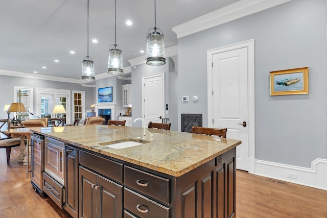 kitchen featuring a fireplace, a sink, dark brown cabinetry, crown molding, and stainless steel microwave