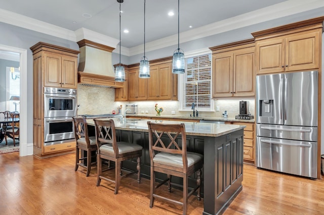 kitchen with an island with sink, a sink, custom range hood, appliances with stainless steel finishes, and light wood-type flooring