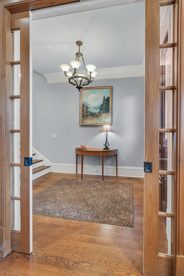 unfurnished dining area with wood finished floors, baseboards, stairs, crown molding, and a notable chandelier