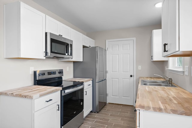 kitchen with wood tiled floor, butcher block counters, appliances with stainless steel finishes, white cabinets, and a sink