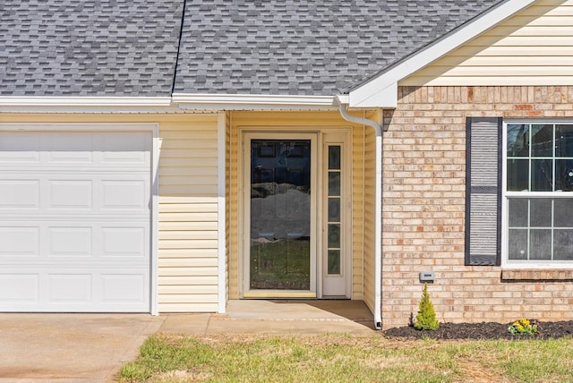 view of exterior entry featuring a garage, brick siding, mansard roof, and a shingled roof