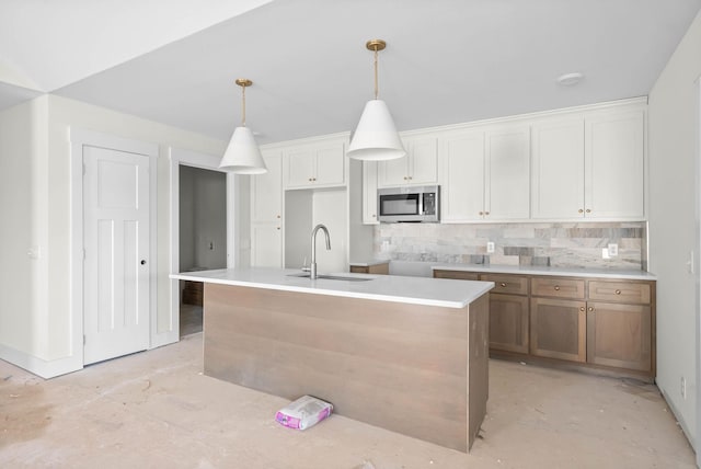 kitchen with stainless steel microwave, pendant lighting, decorative backsplash, white cabinetry, and a sink