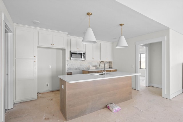 kitchen featuring stainless steel microwave, a center island with sink, pendant lighting, white cabinets, and a sink