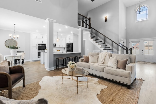 living room with visible vents, stairs, light wood-style flooring, an inviting chandelier, and ornate columns