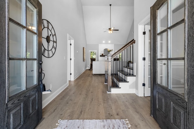 entrance foyer featuring a ceiling fan, wood finished floors, baseboards, high vaulted ceiling, and stairs