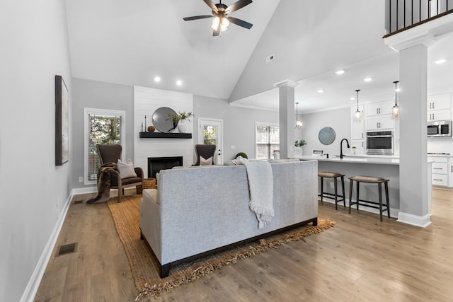 living area featuring visible vents, light wood-style flooring, a fireplace, and decorative columns