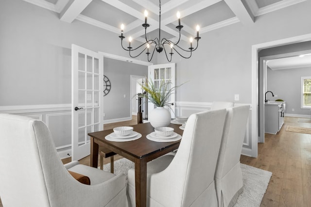 dining area featuring beamed ceiling, ornamental molding, coffered ceiling, light wood finished floors, and baseboards