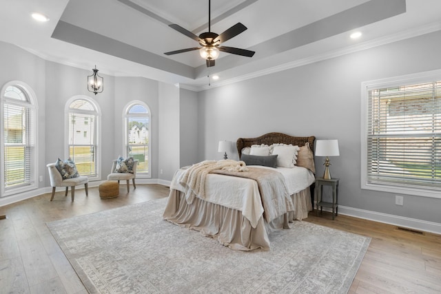 bedroom with a tray ceiling, baseboards, visible vents, and wood finished floors