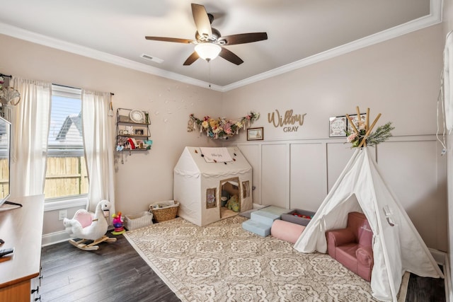 playroom with dark wood-style floors, visible vents, ceiling fan, and ornamental molding