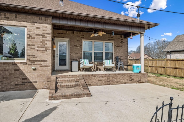 exterior space featuring a ceiling fan, a patio, fence, roof with shingles, and brick siding