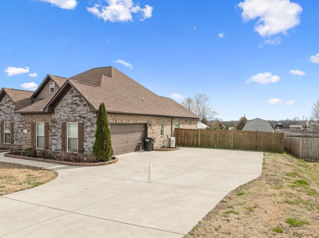 view of side of home with a garage, a shingled roof, driveway, and fence