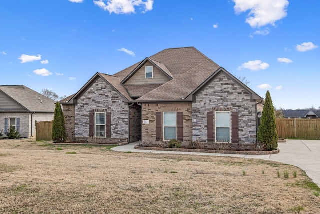 view of front of property featuring stone siding, roof with shingles, a front lawn, and fence