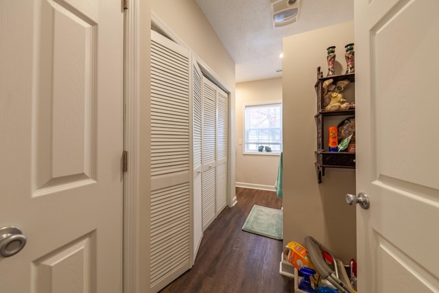 hallway with dark wood-style floors, a textured ceiling, and baseboards