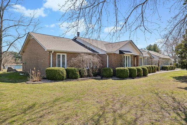 view of property exterior with a yard, brick siding, roof with shingles, and a chimney